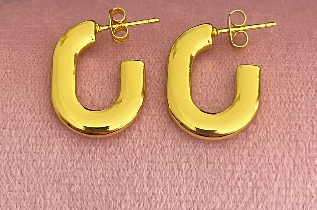 Gold chunky oval hoop earrings laid flat on pink velvet surface