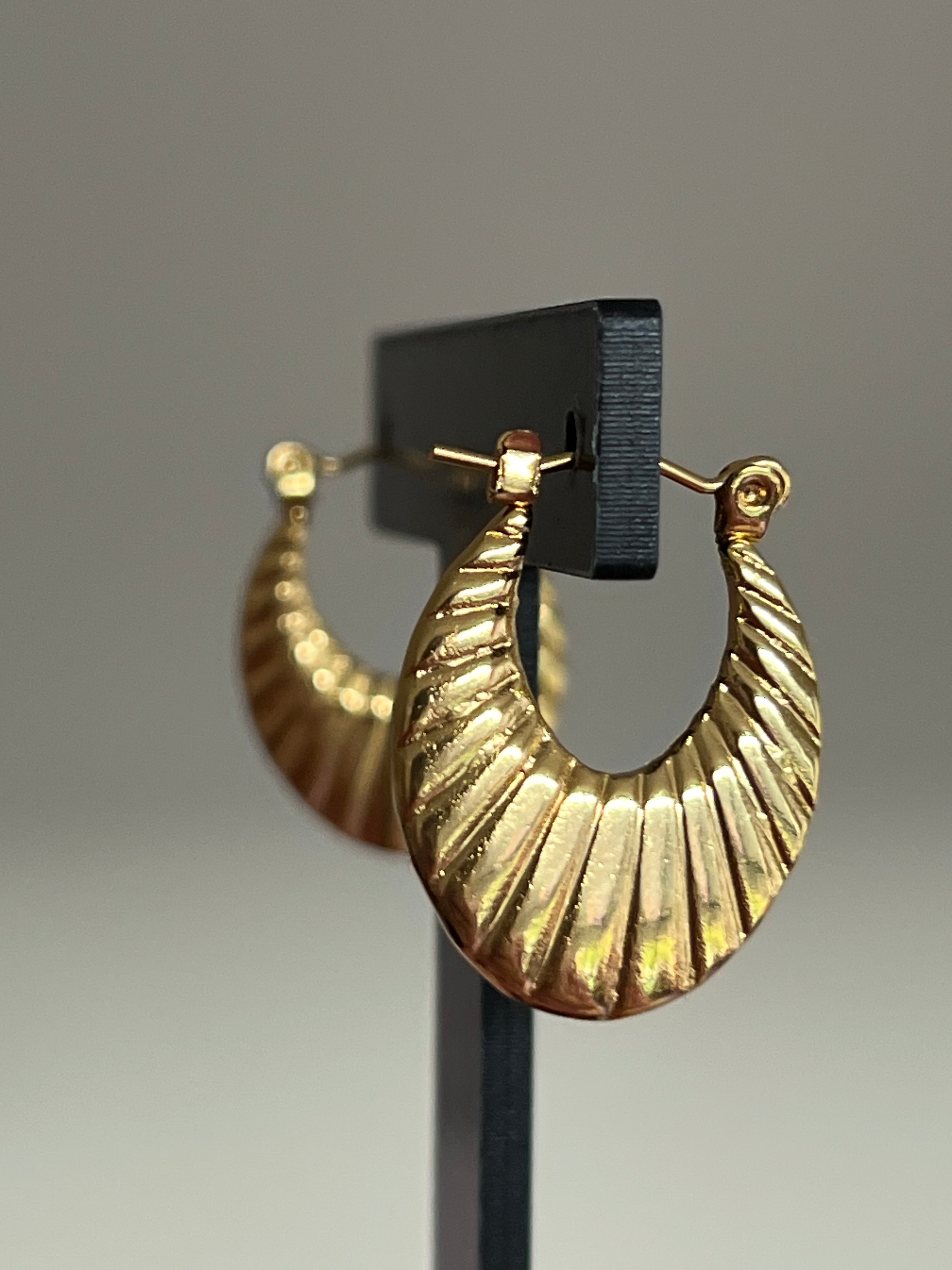 Gold ribbed crescent hoop earrings on black jewellery stand