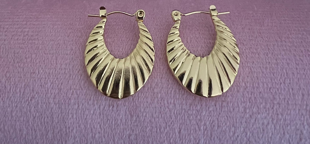 Gold ribbed crescent hoop earrings laid flat on pink velvet surface