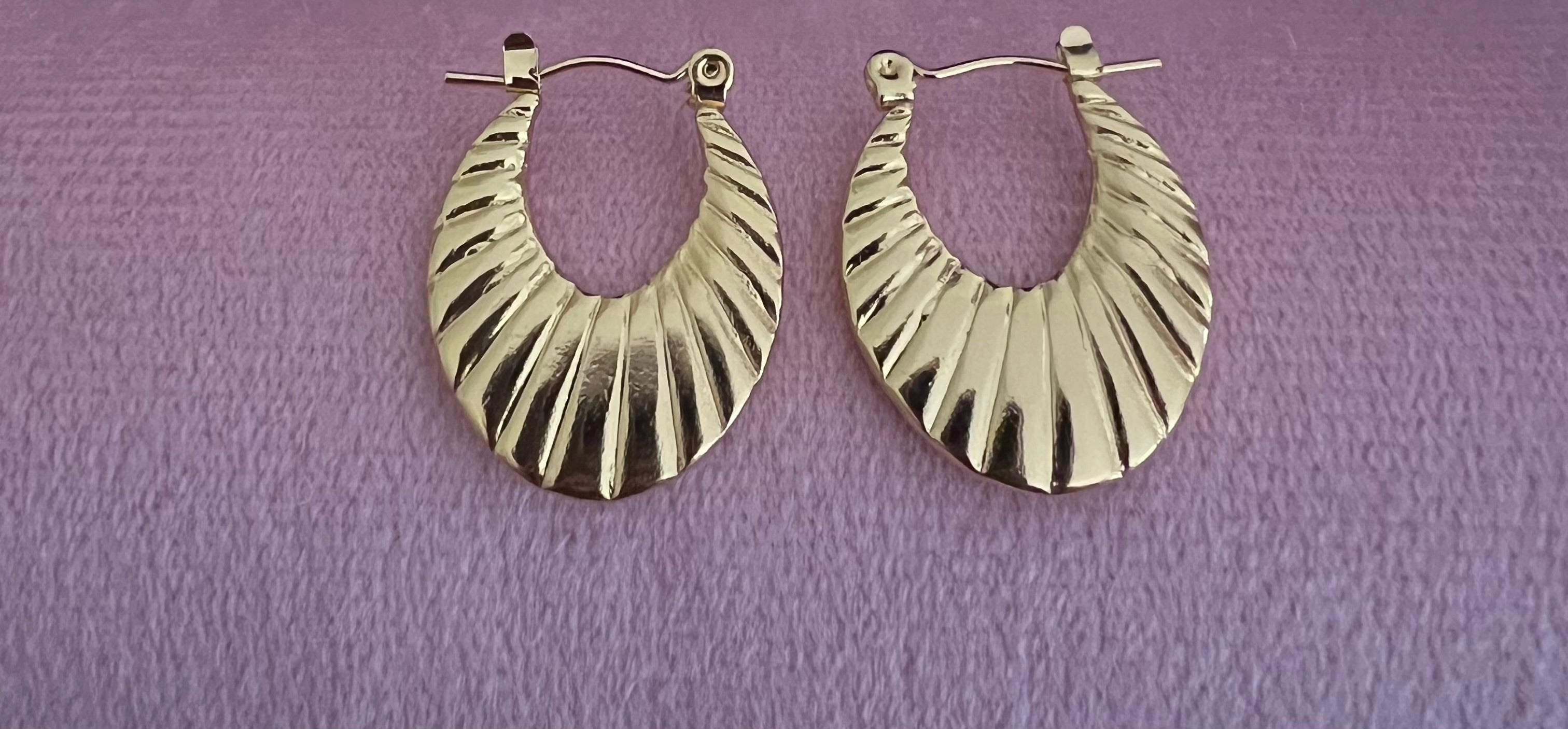 Gold ribbed crescent hoop earrings laid flat on pink velvet surface