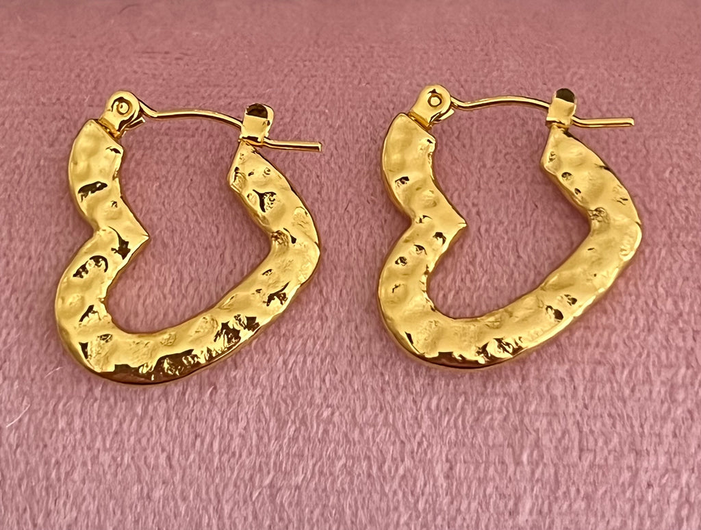 Gold hammered heart hoop earrings laid flat on pink velvet surface