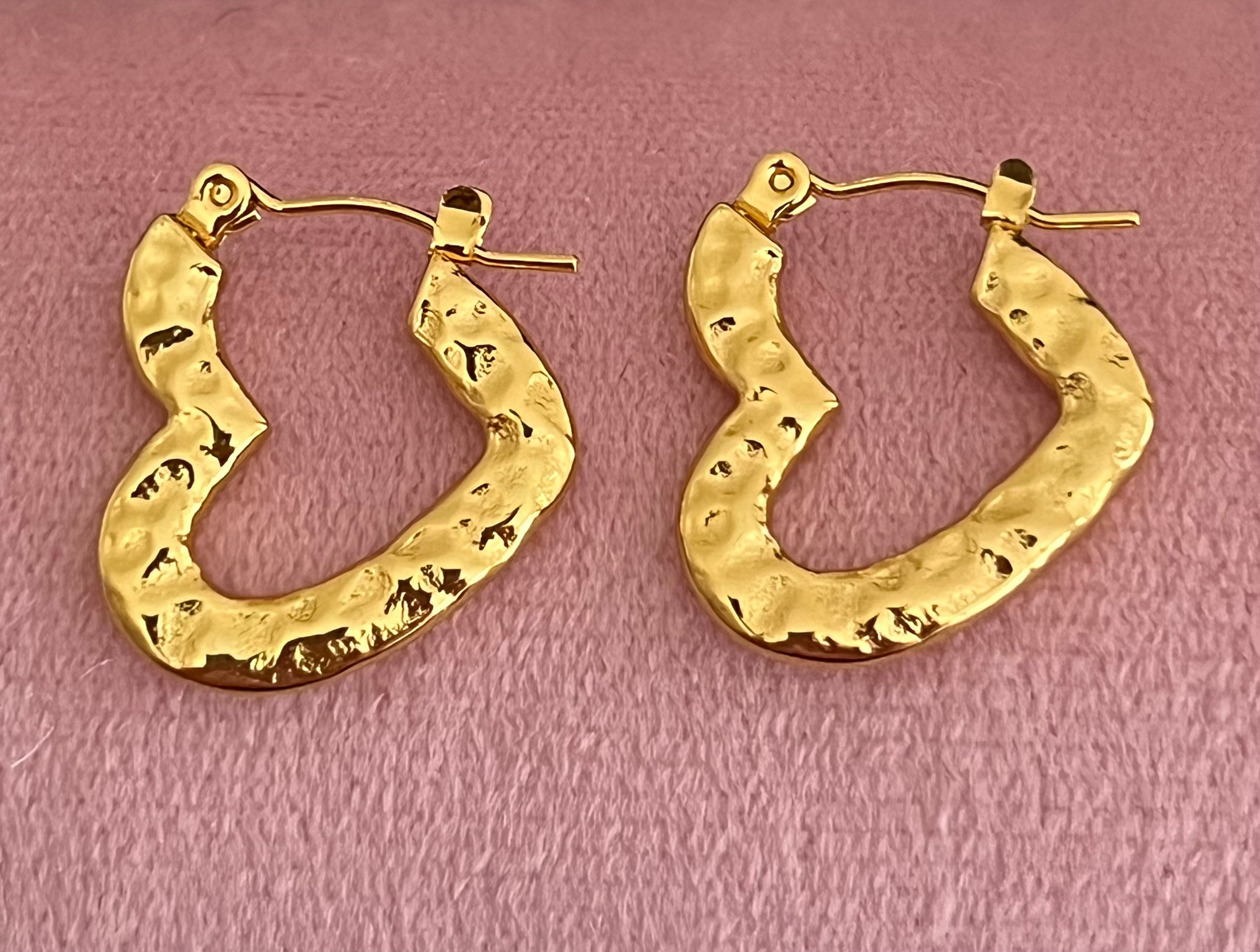Gold hammered heart hoop earrings laid flat on pink velvet surface
