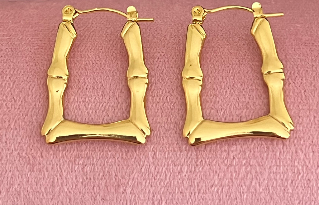 Gold bamboo square hoop earrings laid flat on pink velvet surface