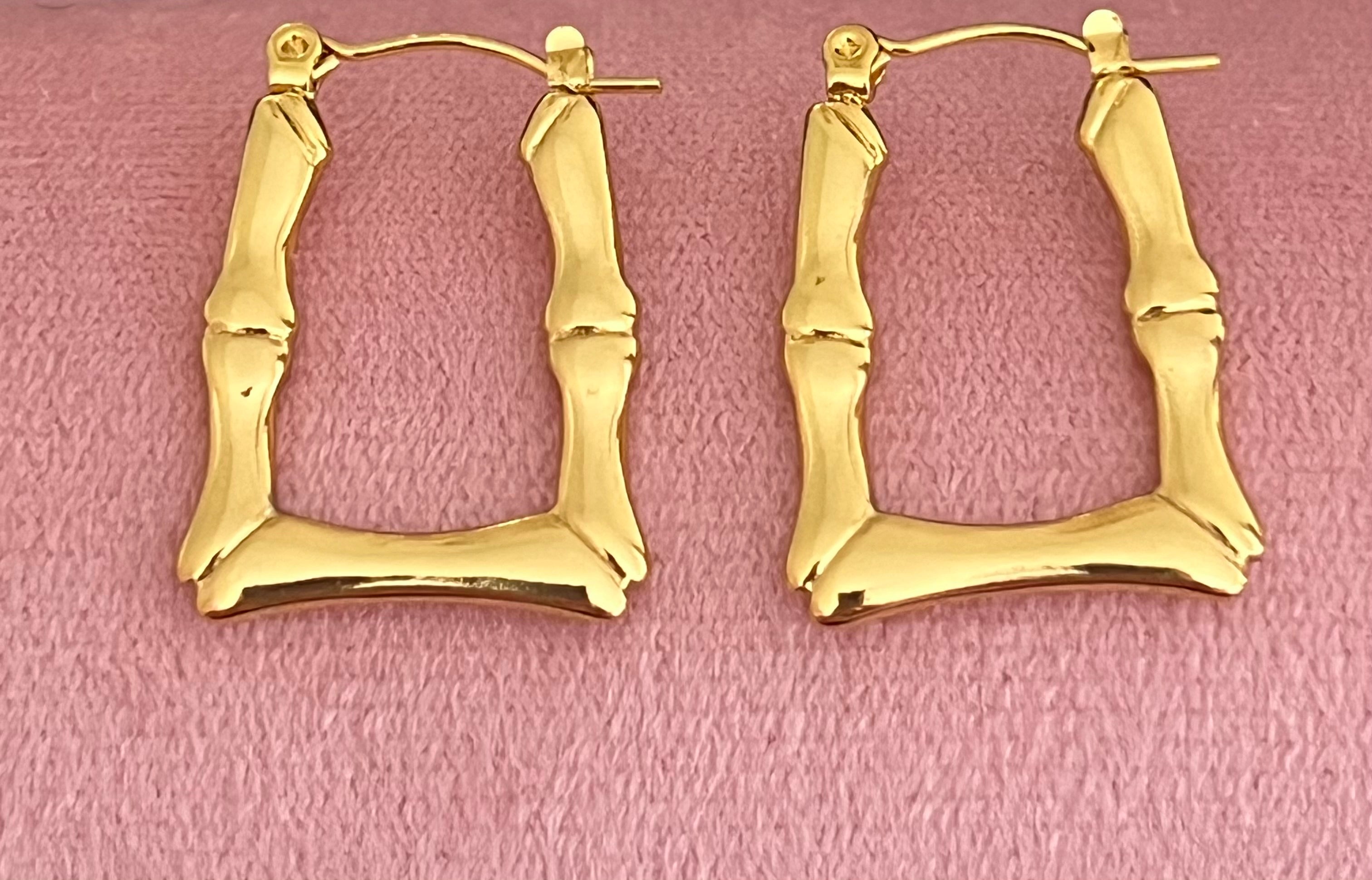 Gold bamboo square hoop earrings laid flat on pink velvet surface