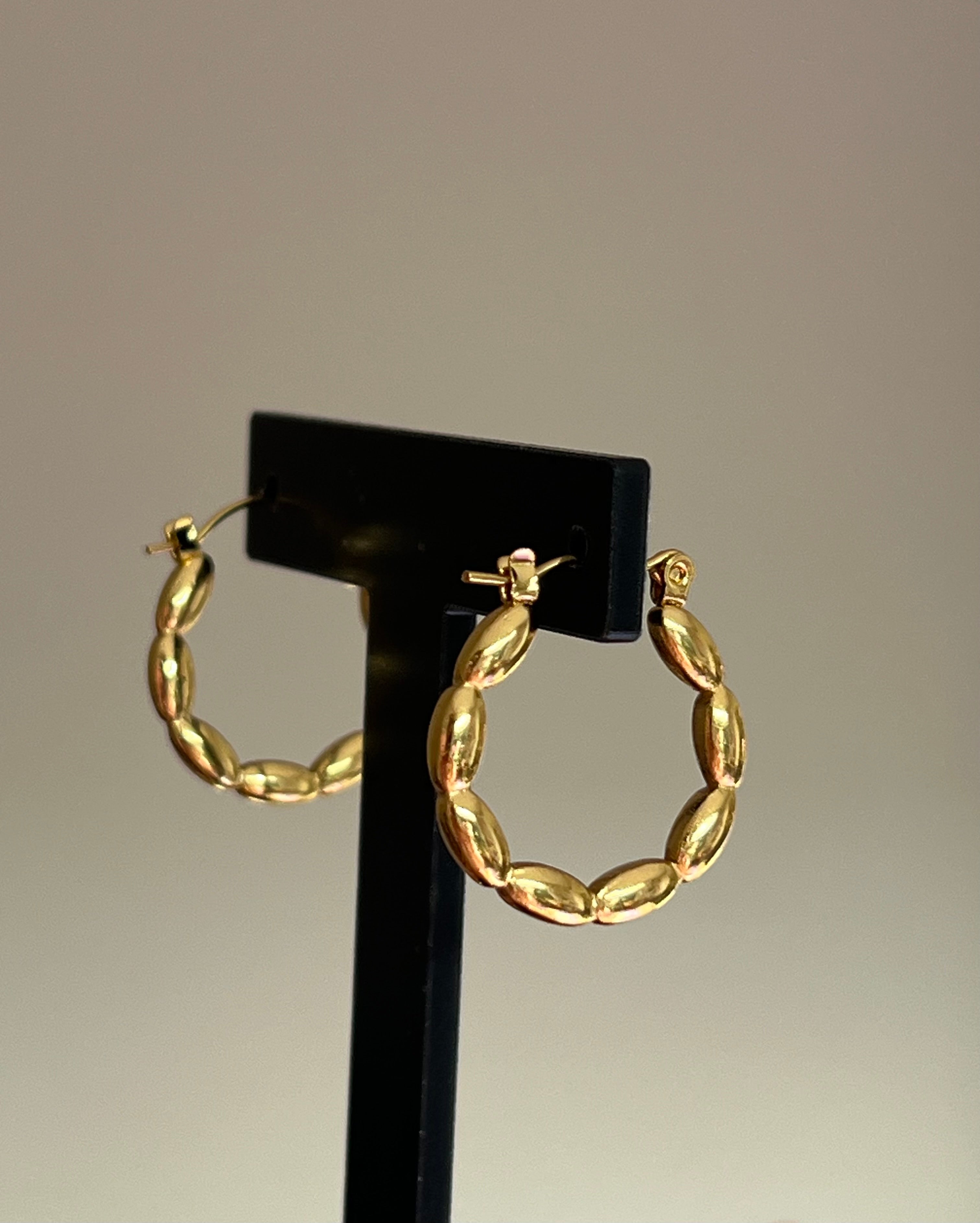 Gold beaded hoop earrings displayed on black jewellery stand