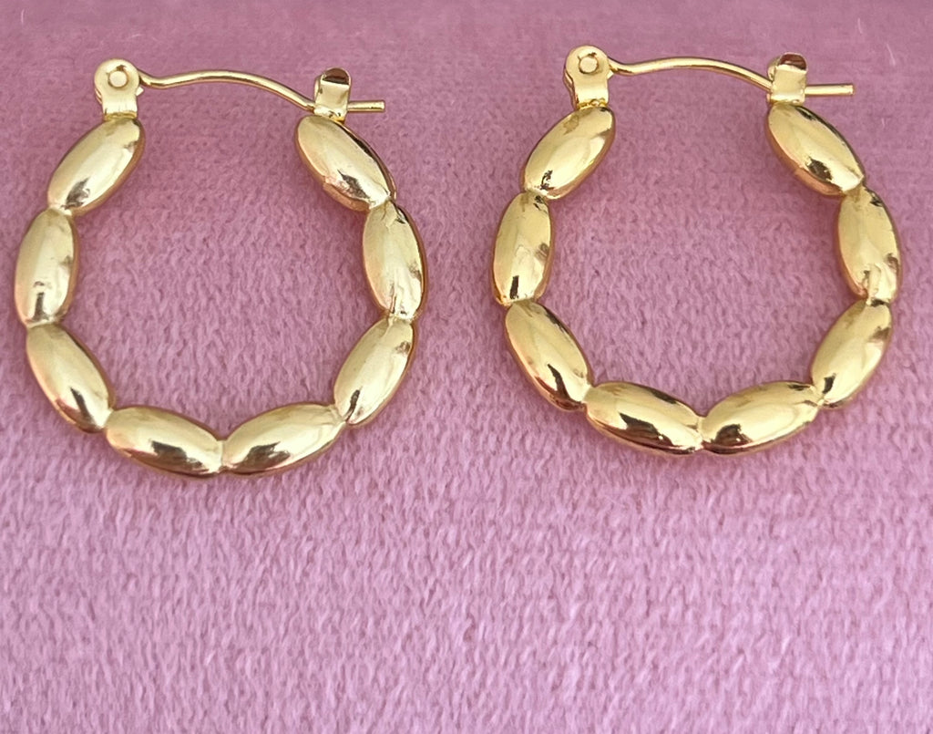 Gold beaded hoop earrings laid flat on pink velvet surface