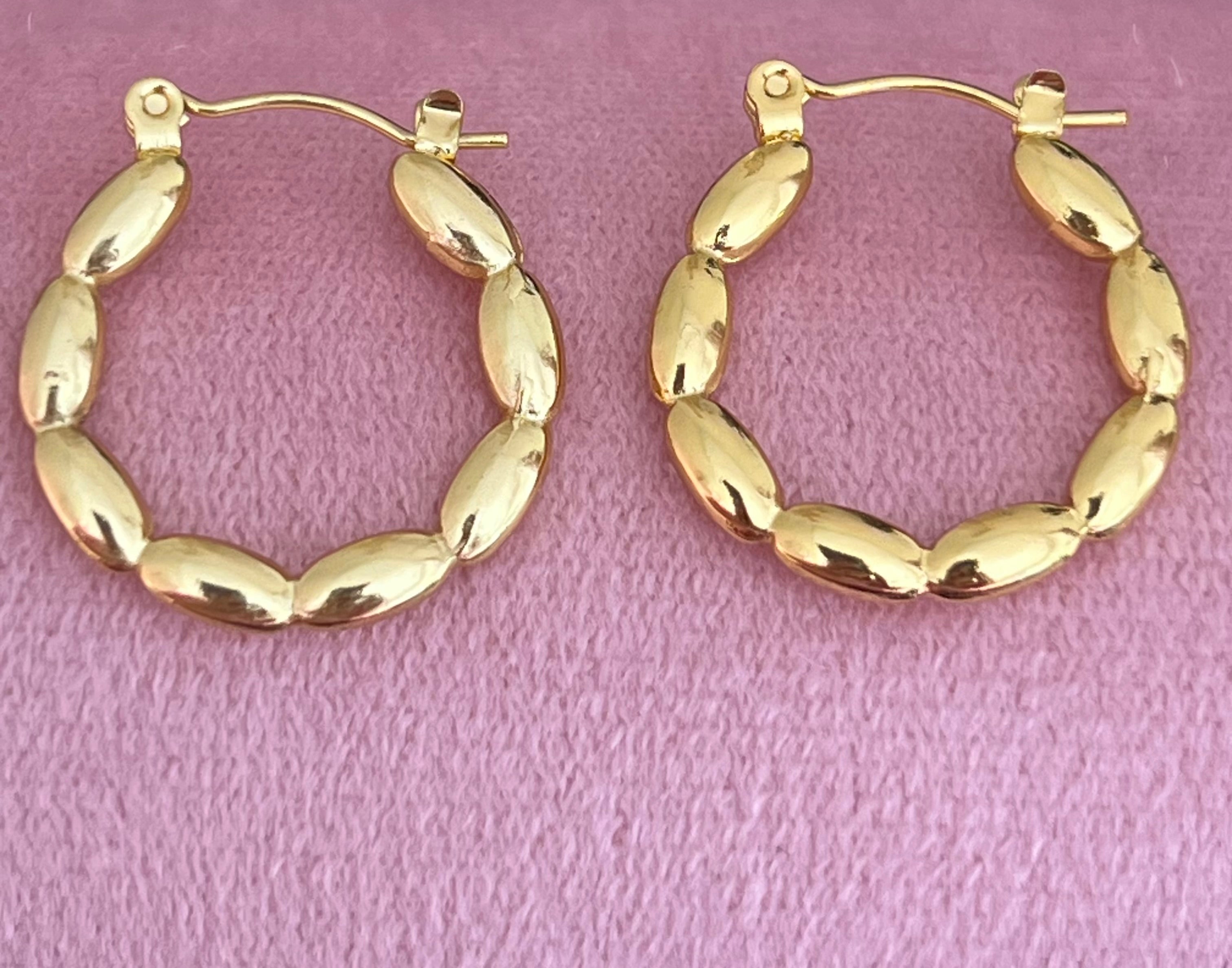 Gold beaded hoop earrings laid flat on pink velvet surface