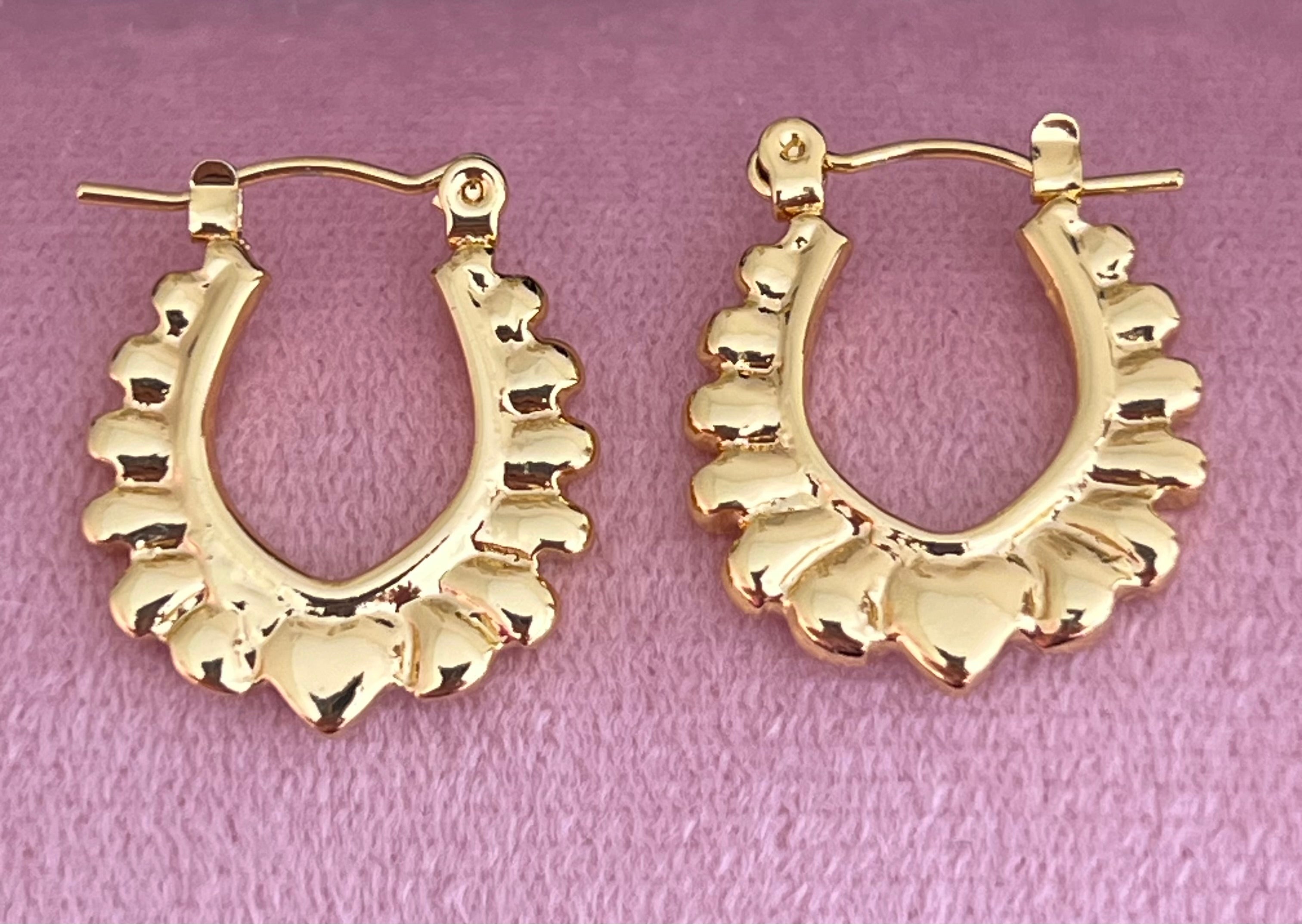 Gold scalloped heart hoop earrings laid flat on pink velvet surface