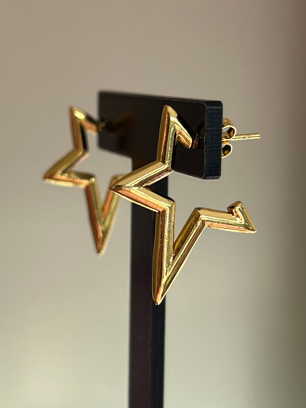 Gold star stud earrings laid flat on pink velvet surface